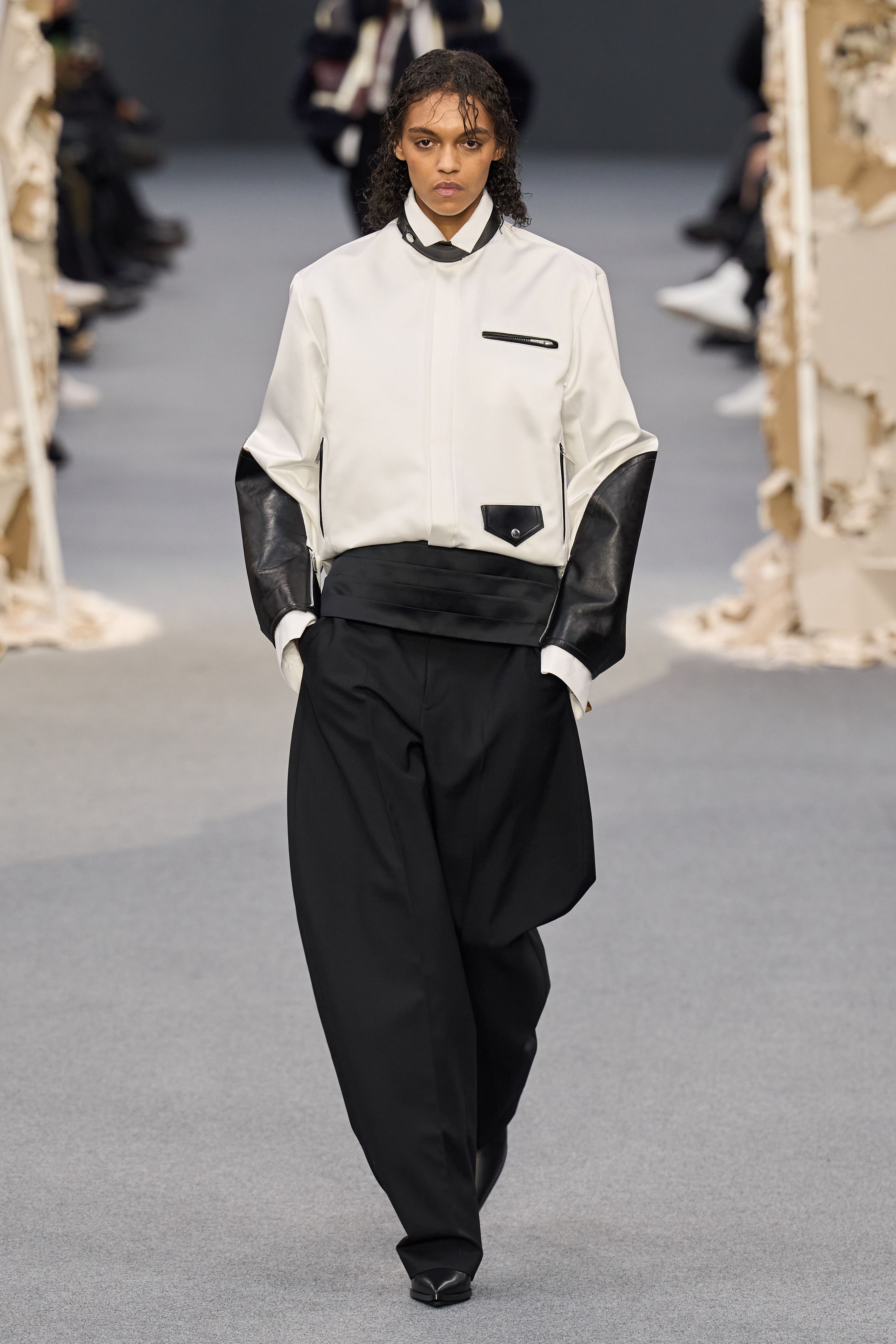 Sacai 2026秋冬再次展示其无可复制的“混合美学”。正装、牛仔、皮草与制服元素被高度结构化地拼接，形成既熟悉又陌生的服装形态。性别边界被进一步模糊，层叠结构制造流动节奏，使行走本身成为设计的一部分。系列在秩序与混乱之间找到平衡，是Sacai 对当代复杂生活状态的持续回应-顽石频道趋势研究